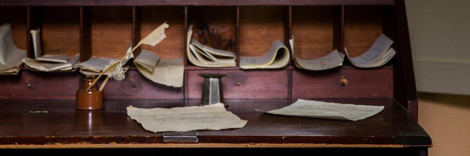 A desk with notes, papers, and quill pens