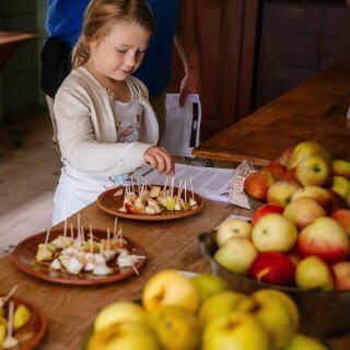 A child picks up a piece of apple off of a redware plate to sample