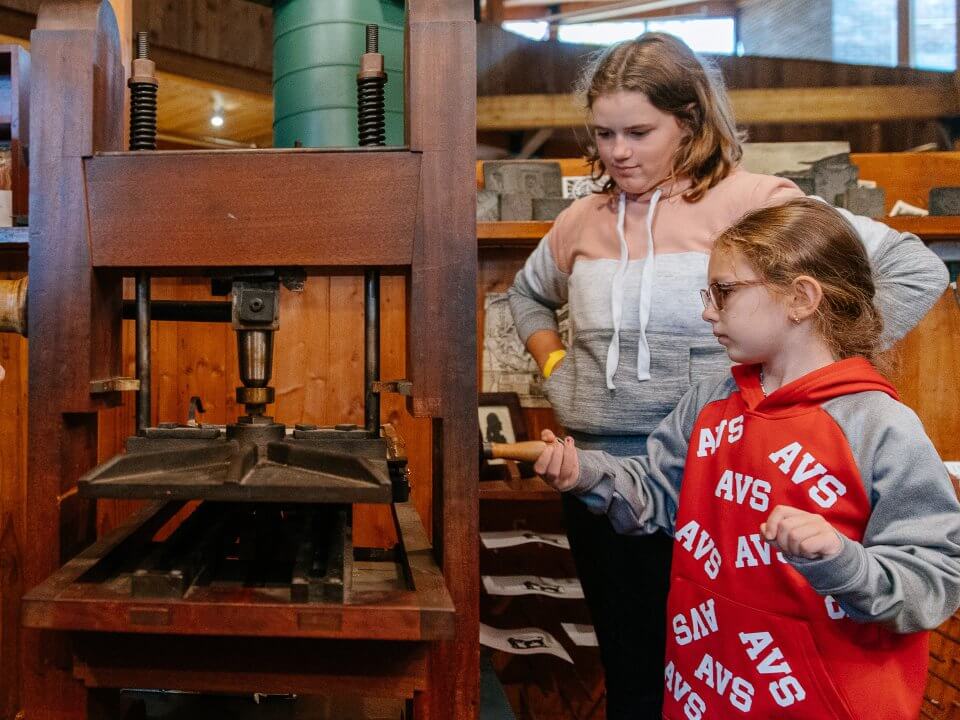 Two kids learn how to use an old fashioned printing press