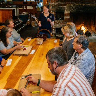 People gathered around a table listening to an instructor give directions for a hearth cooking workshop