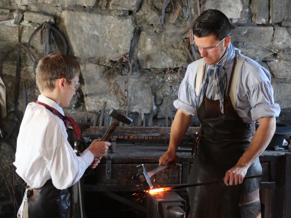A Discovery Adventures Camper works with a Costumed Historian in the Blacksmith Shop