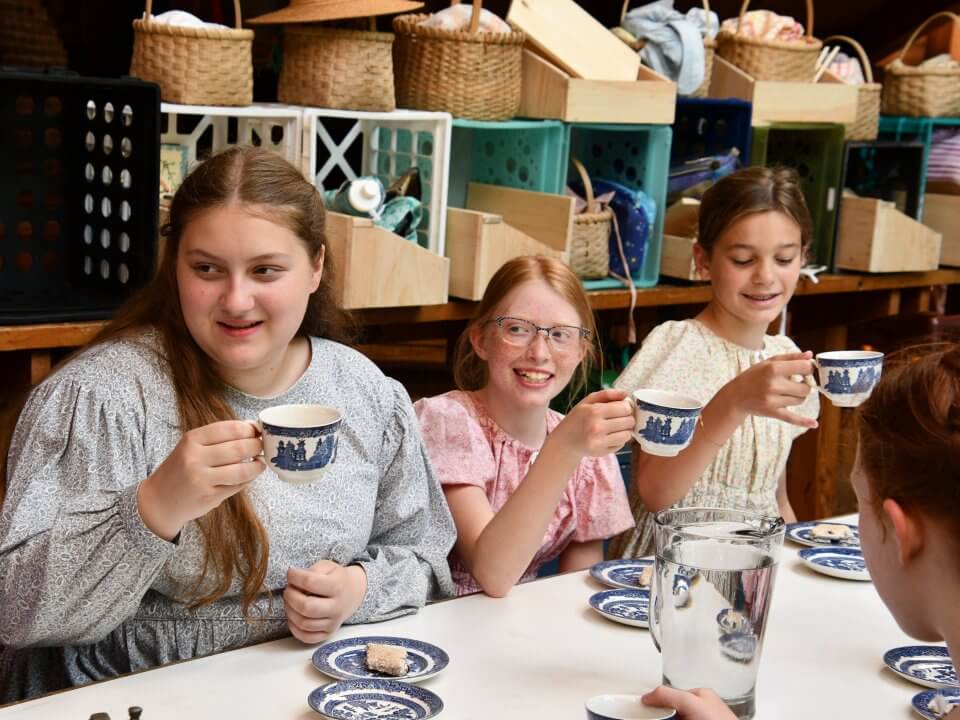 Three girls in dresses sip tea from fine china
